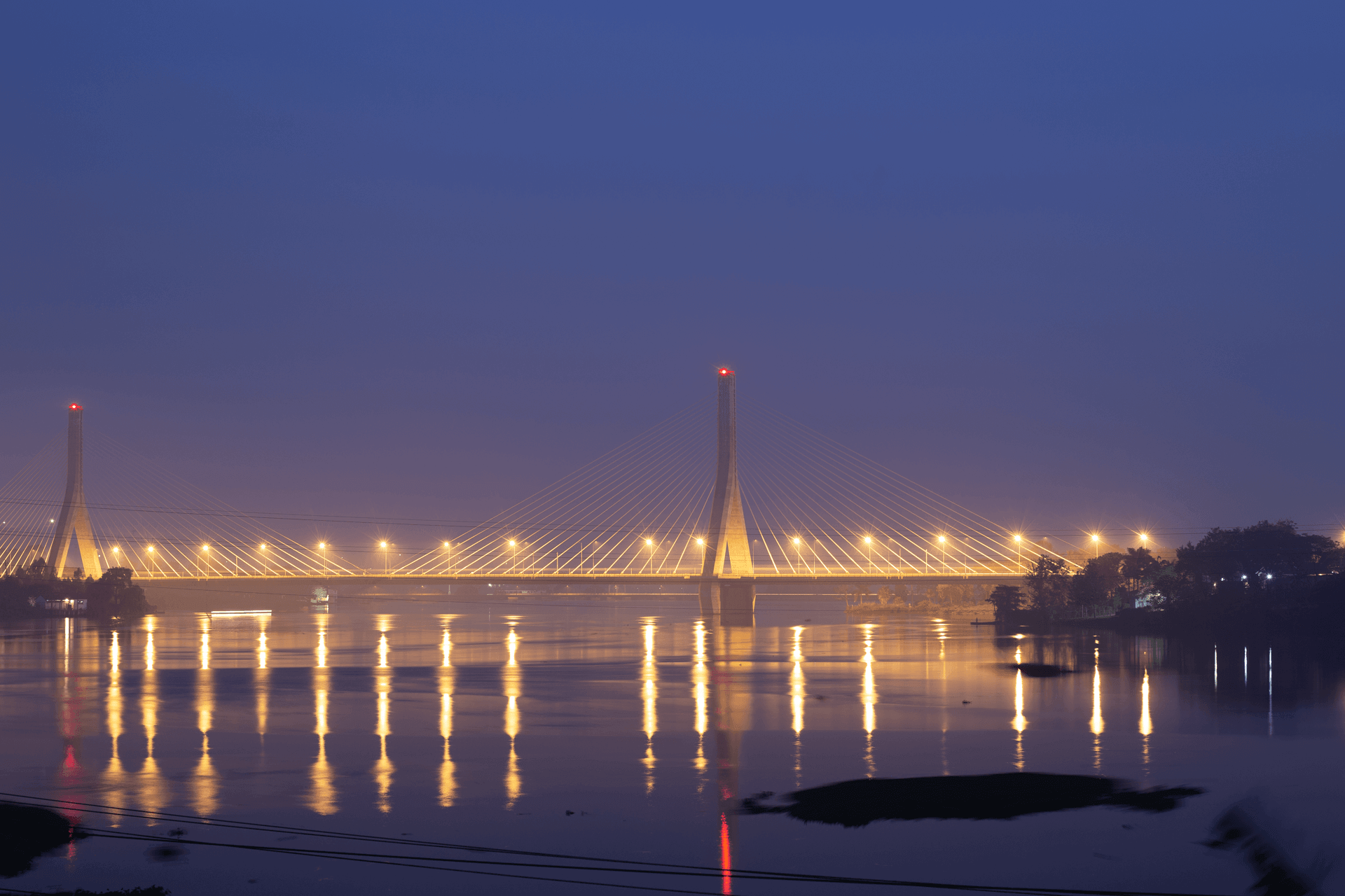 Illuminated cable-stayed bridge reflected in water at dusk